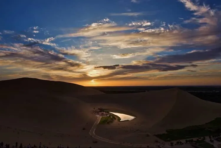 A serene twilight view of Crescent Moon Lake nested inside the towering golden dunes of Dunhuang