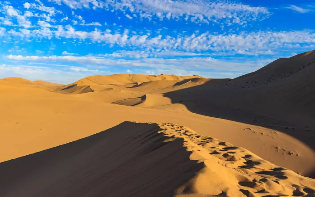 Golden summer sunlight illuminating the vast desert dunes of Dunhuang during peak travel season