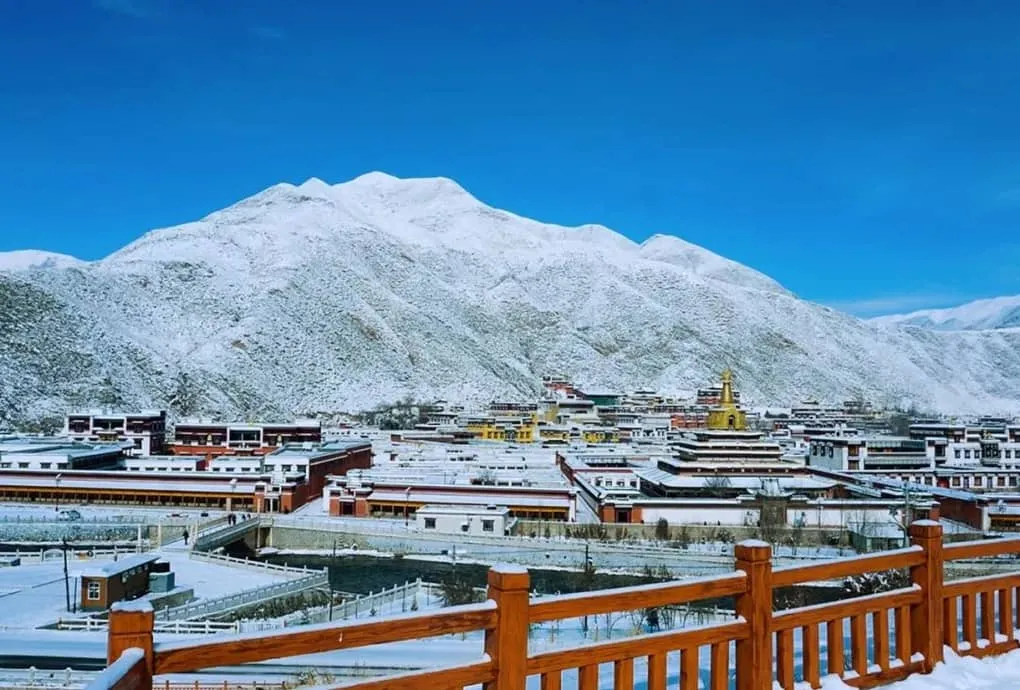 Snow dusting the ancient red cliffs and rooftops of a quiet winter monastery in southern Gansu