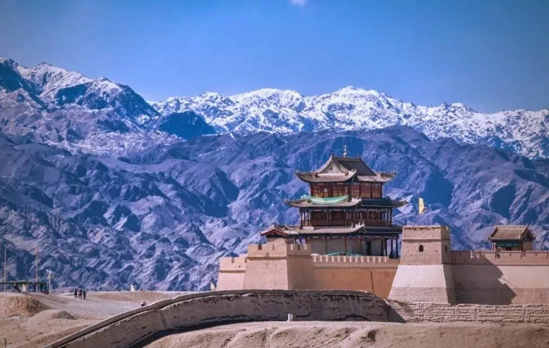 A telephoto view compressing the earthen ramparts of Jiayuguan against the massive snow-capped Qilian mountain range