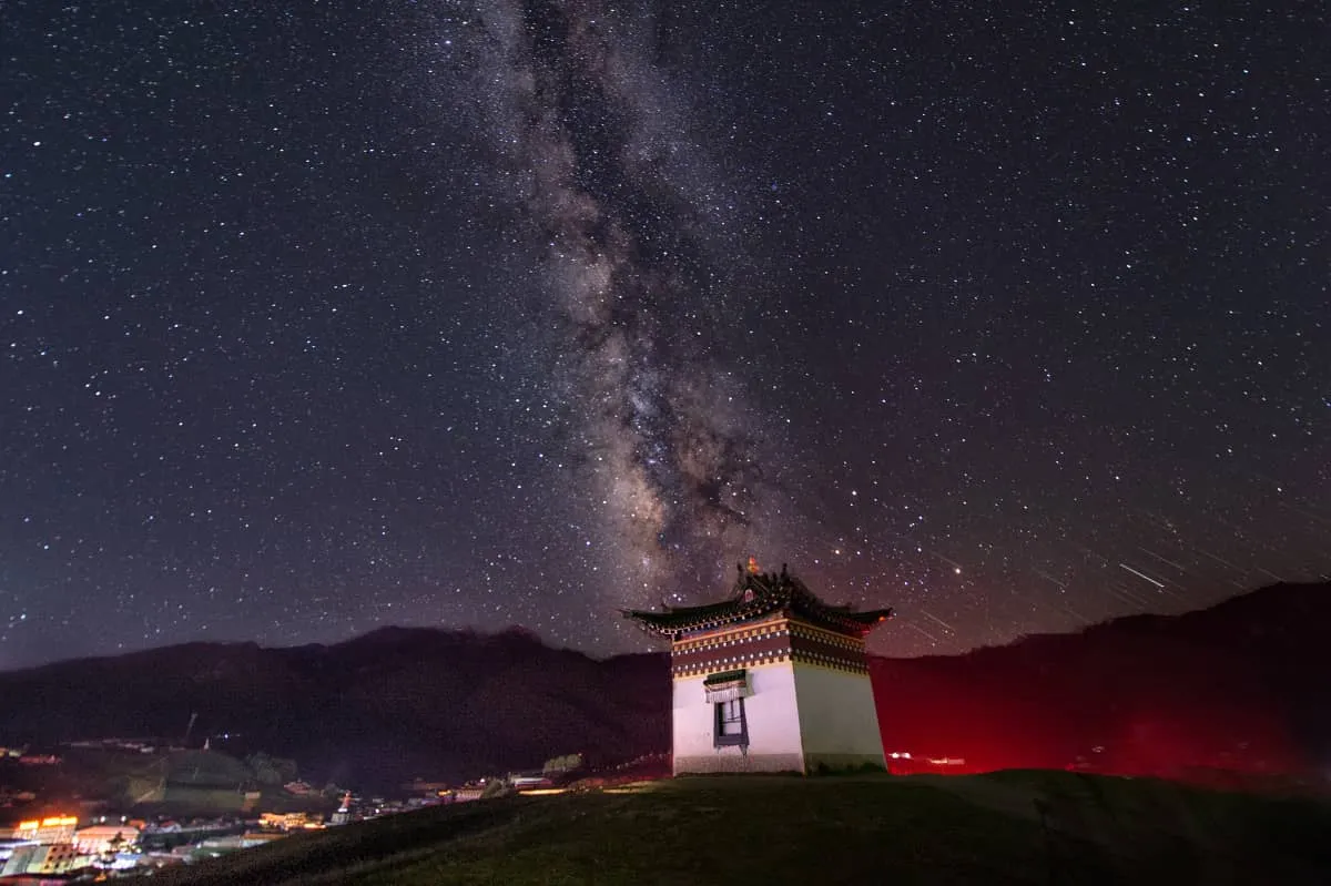 The brilliant core of the Milky Way arcing across the night sky over a golden Tibetan pagoda in Langmusi
