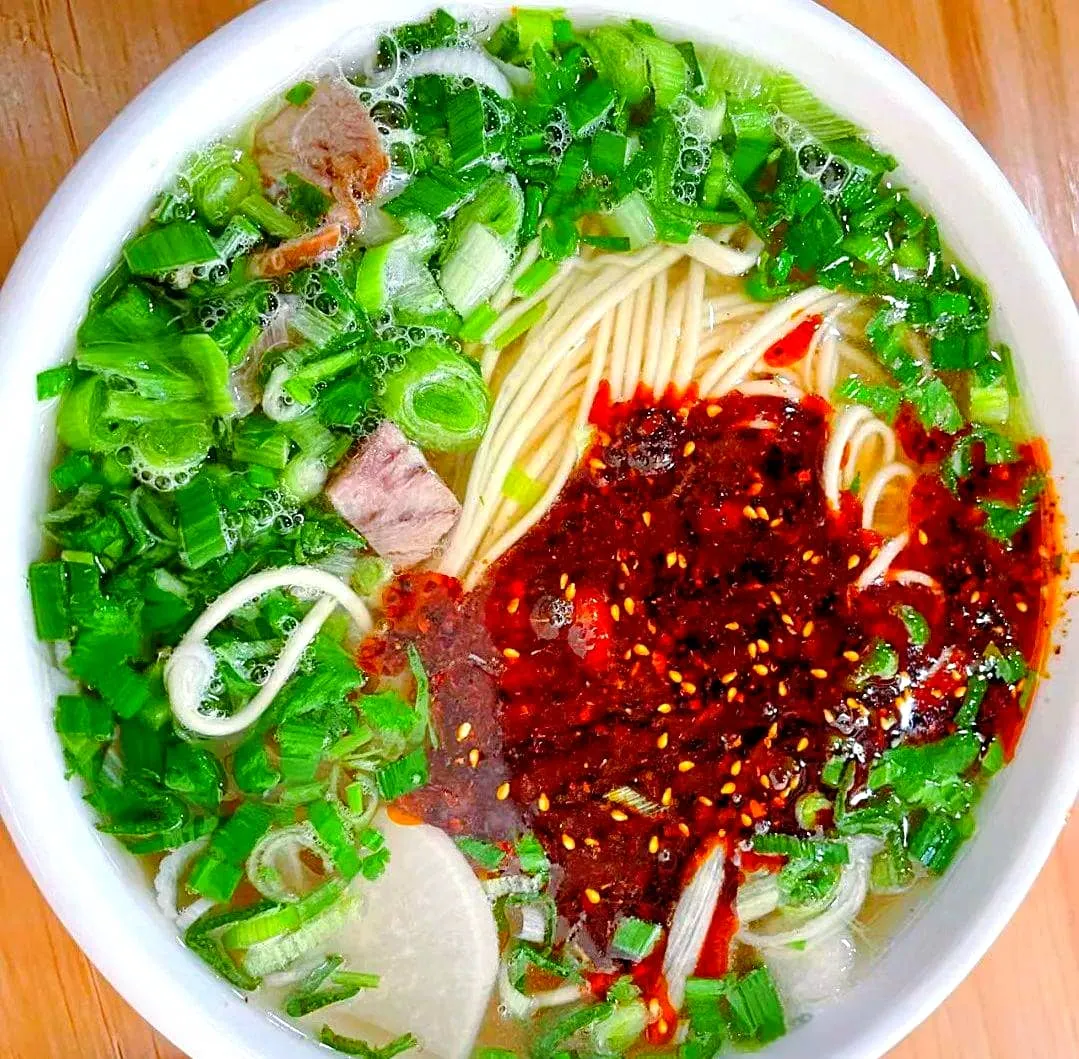 A perfectly prepared bowl of authentic Lanzhou beef noodles displaying bright red chili oil and fresh green cilantro