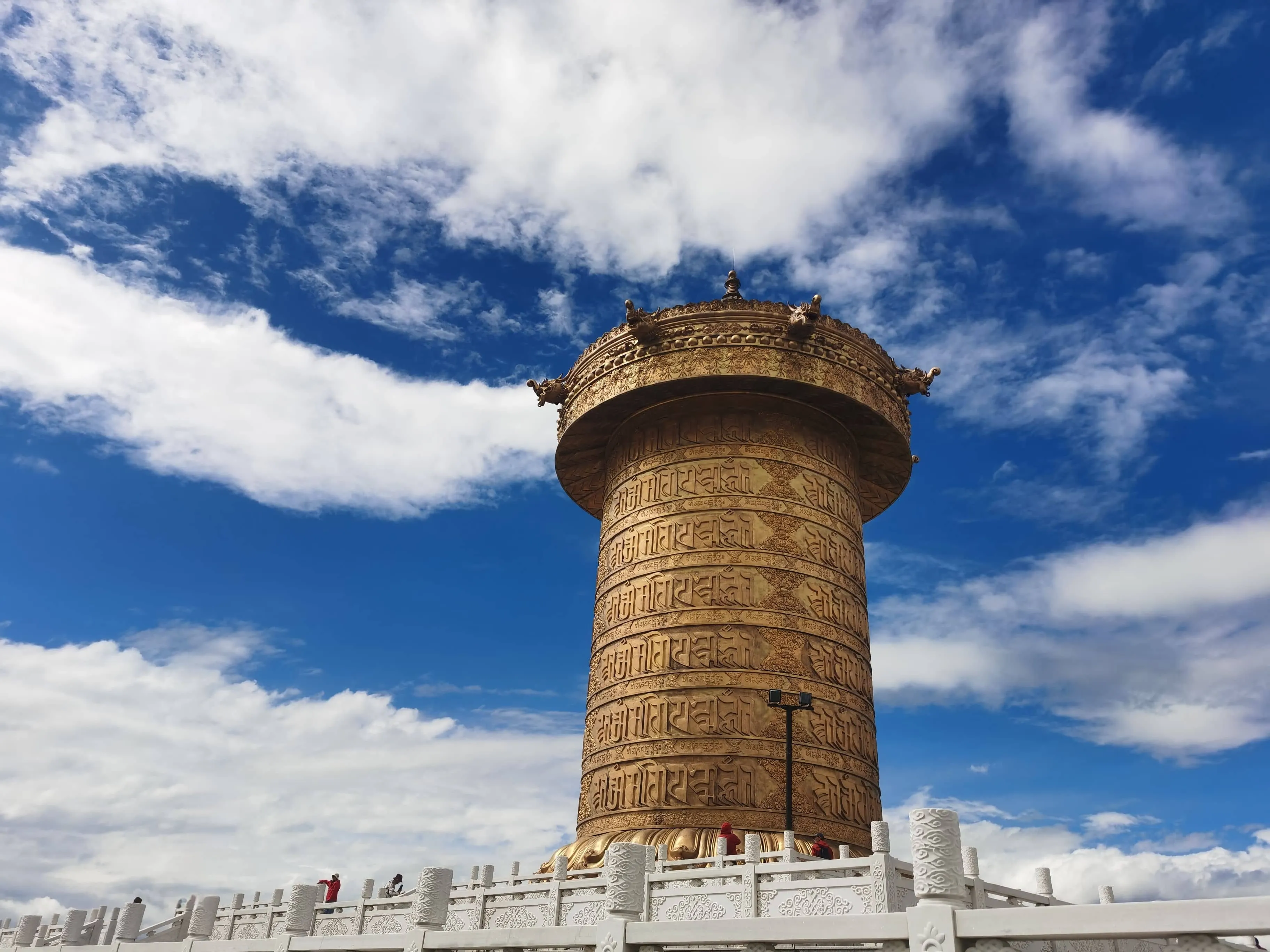An international traveler respectfully walking clockwise past a massive row of golden Tibetan prayer wheels