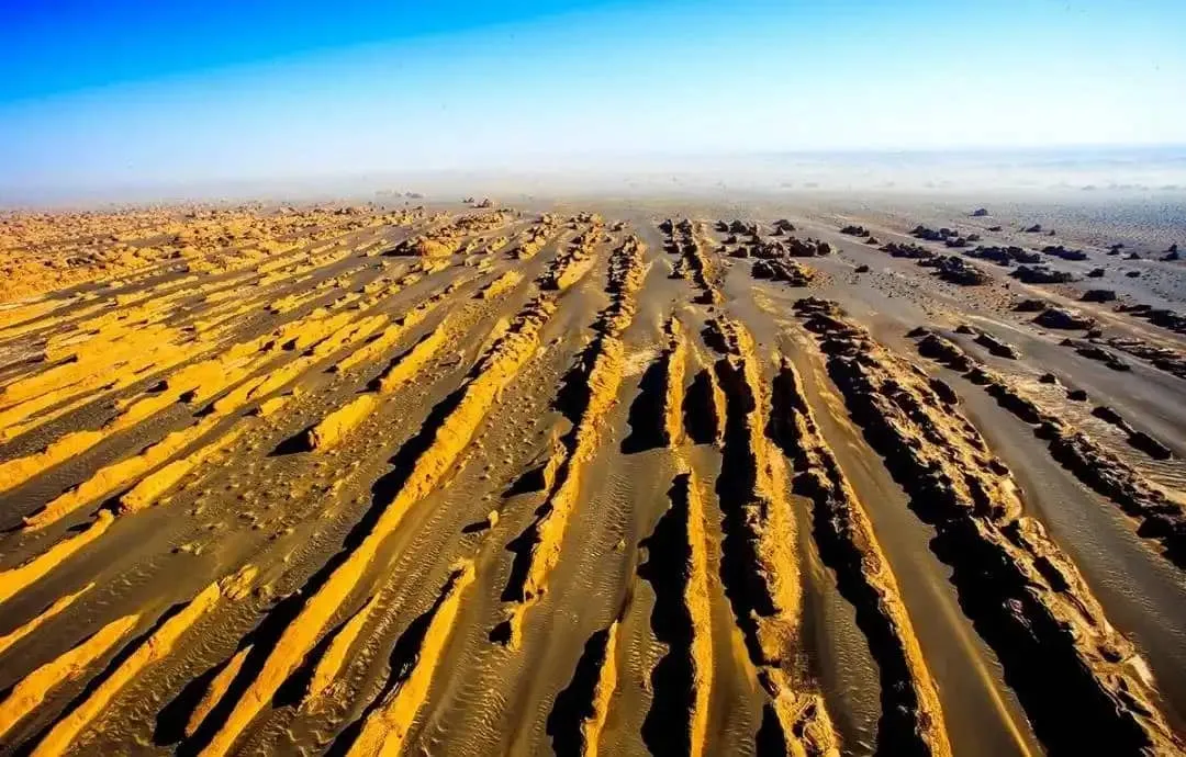 A massive clay Yardang rock formation shaped like a majestic battleship floating on a sea of black Gobi gravel