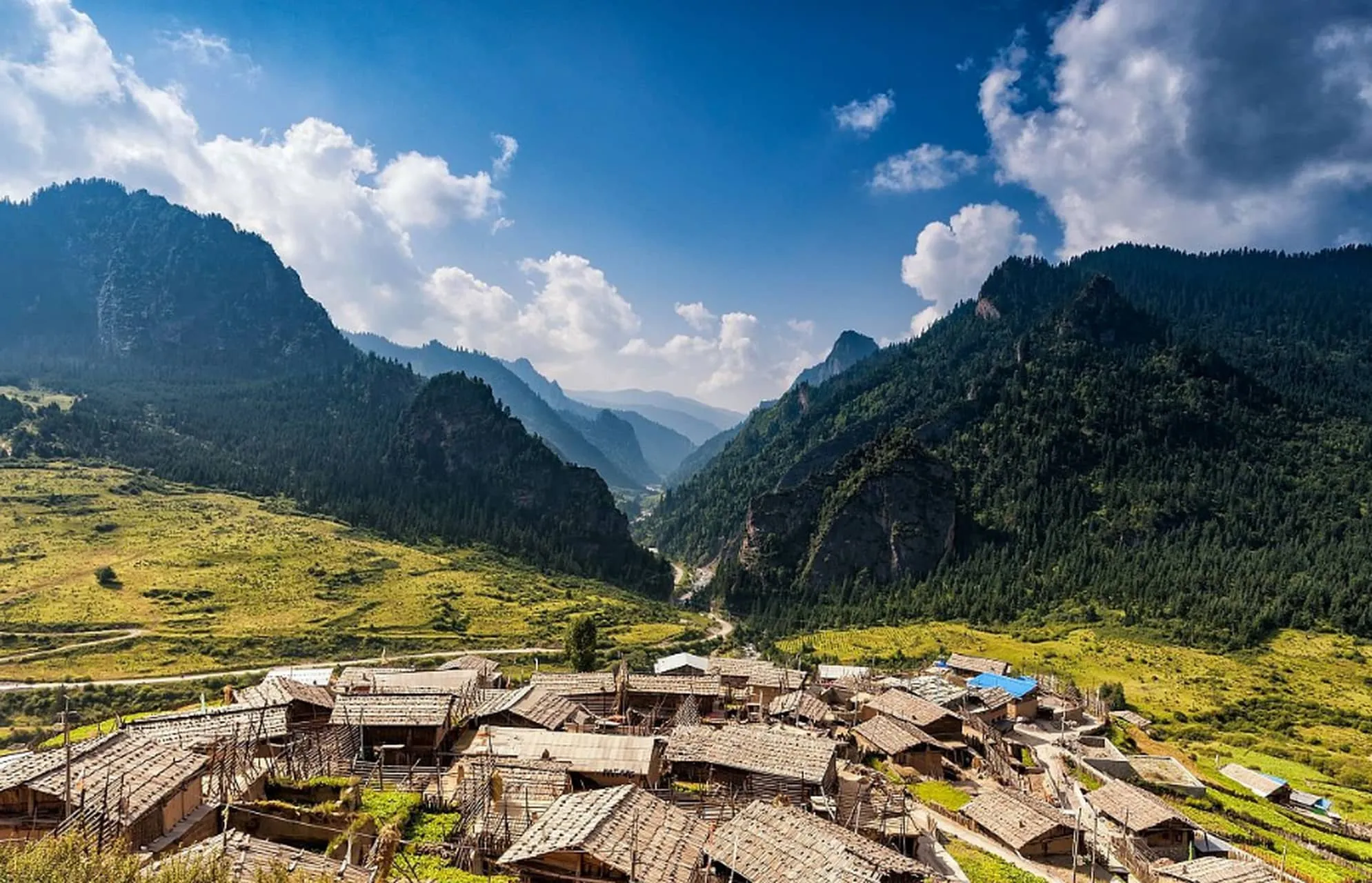 The mist-shrouded limestone towers of Zagana overlooking traditional Tibetan wooden houses